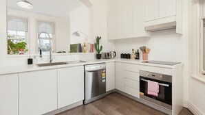 A modern kitchen with white cabinetry, a dishwasher, an oven, a window with a view, and a plant. - Stunning Sydney Home 9 (Millers Point)