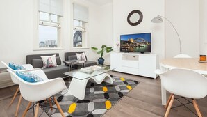 A modern living room with a glass coffee table, a sofa, a TV, and a cityscape view. - Stunning Sydney Home 9 (Millers Point)