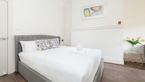 A neatly made bed with white linens, a grey upholstered headboard, and a floral pillow. - Stunning Sydney Home 9 (Millers Point)