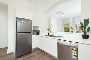 A modern kitchen with white cabinets, a stainless steel refrigerator, a microwave, a sink, and a dishwasher. - Stunning Sydney Home 9 (Millers Point)