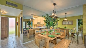Un'ampia sala da pranzo con tavoli e panche in legno, una cucina sullo sfondo e una pianta grande al centro.