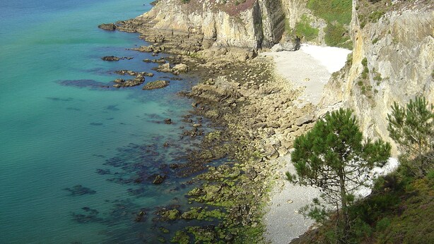 A coastal landscape with rocky cliffs, clear blue waters, and a distant shoreline with buildings.