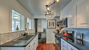 Una cocina moderna con armarios blancos, encimera negra, pileta de acero inoxidable, estufa y microondas.