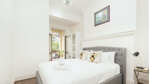 A neatly made bed with a grey headboard, a bedside table with a lamp, and a framed picture on the wall.