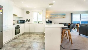 Una cocina moderna con armarios blancos, un microondas y un horno. Cuenta con un comedor con una mesa y sillas.