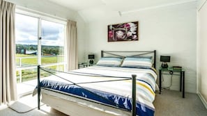 A bedroom with a bed, two bedside tables, a window with curtains, and a painting on the wall.