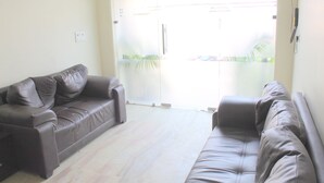 A living room with two leather sofas, a glass door leading outside, and a light-colored floor. - Hotel South Delhi Inn (New Delhi)