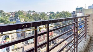 A balcony with a metal railing overlooking a densely populated urban area with various buildings and shops. - Hotel South Delhi Inn (New Delhi)