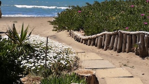 Une promenade en bord de mer, agrémentée d’une clôture en bois, d’escaliers et de verdure, qui mène à la plage.