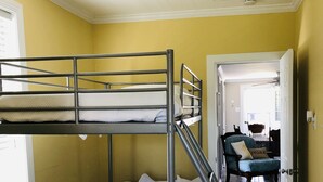 Una cama litera en una habitación con paredes amarillas, un ventilador de techo y vistas a otra habitación con una silla y una mesa.