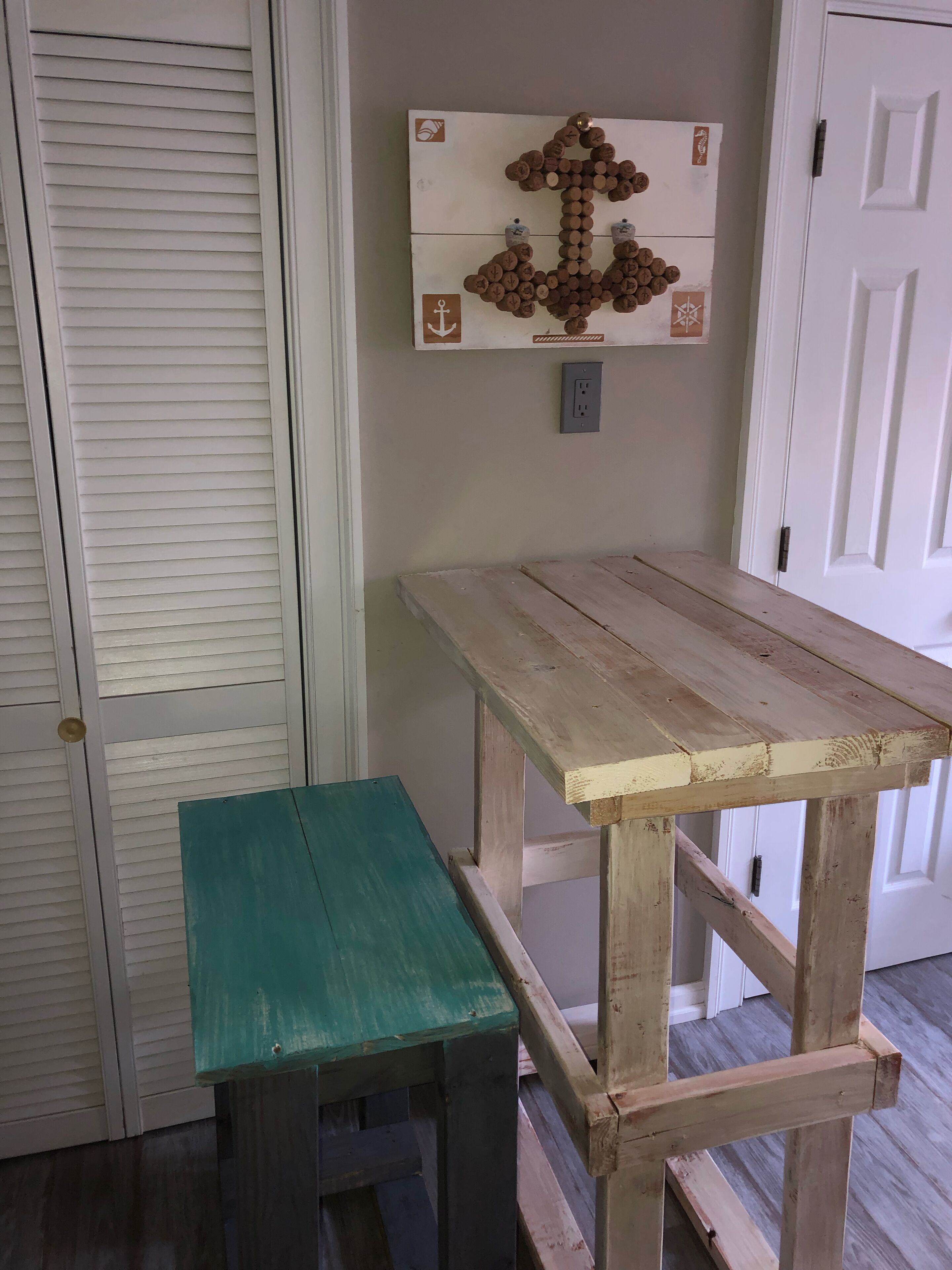 A wooden table with a bench, a wall-mounted cork art piece, and a door with a handle.