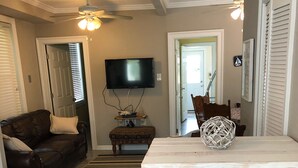 Una sala de estar con un sofá de cuero marrón oscuro, una mesa blanca con una cesta tejida, un televisor de pantalla plana montado en la pared y un banco de madera.