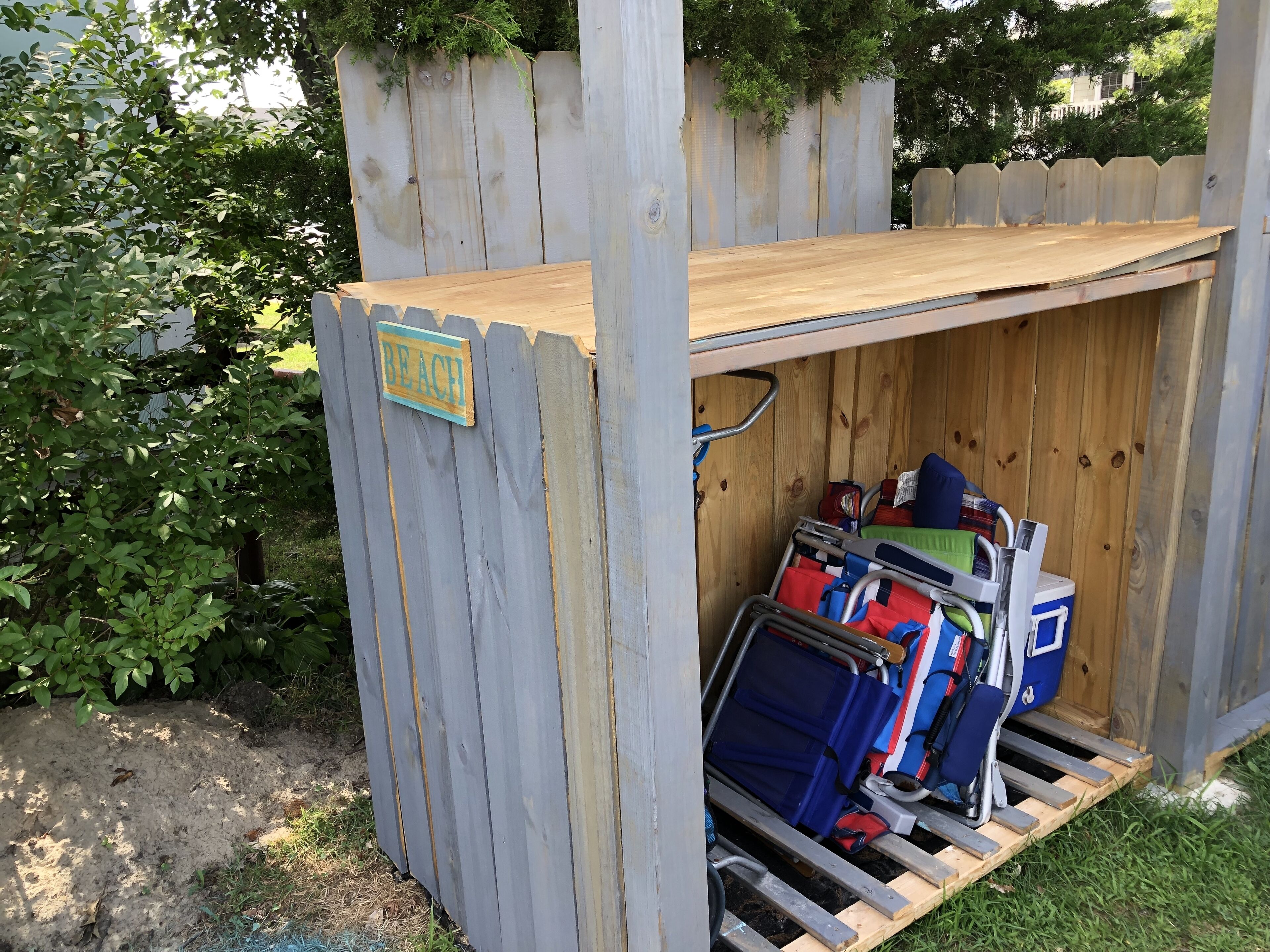 A small wooden structure with a 'BEACH' sign, containing a metal rack with bags and a cooler.
