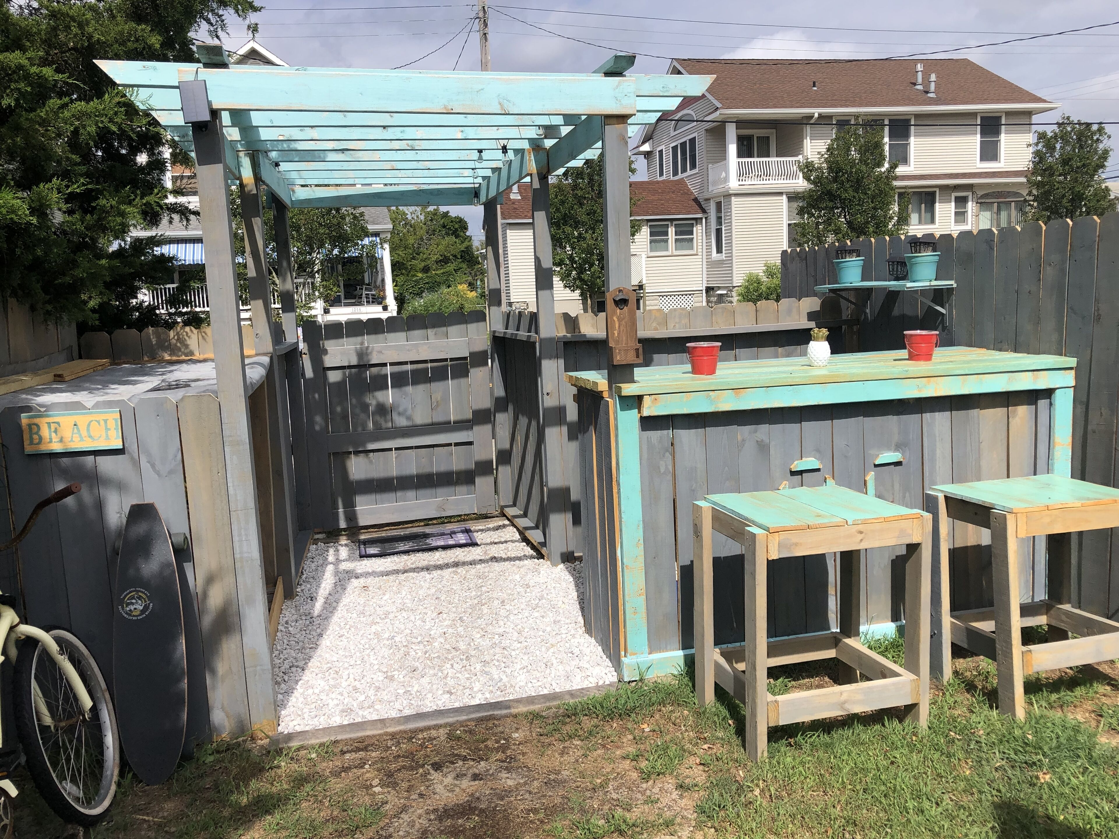 A backyard with a wooden pergola, a barbecue grill, and a small table with chairs.