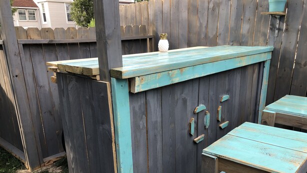 Un espacio de estar al aire libre con encanto, con una mesa y sillas de madera, un pequeño jarrón blanco y una valla de madera al fondo.