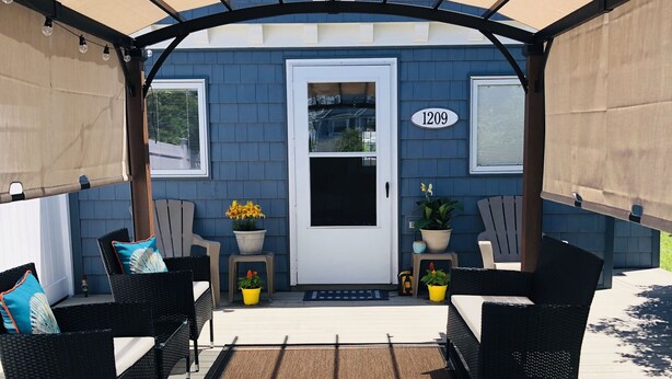 Un patio techado con mobiliario exterior, una puerta con un número y plantas en macetas.