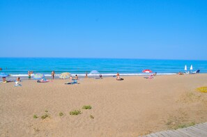A beach with people sunbathing and swimming, umbrellas, and lounge chairs. - Holiday Studio Apartments Yannis on Agios Gordios beach in Corfu (Agios Gordios)