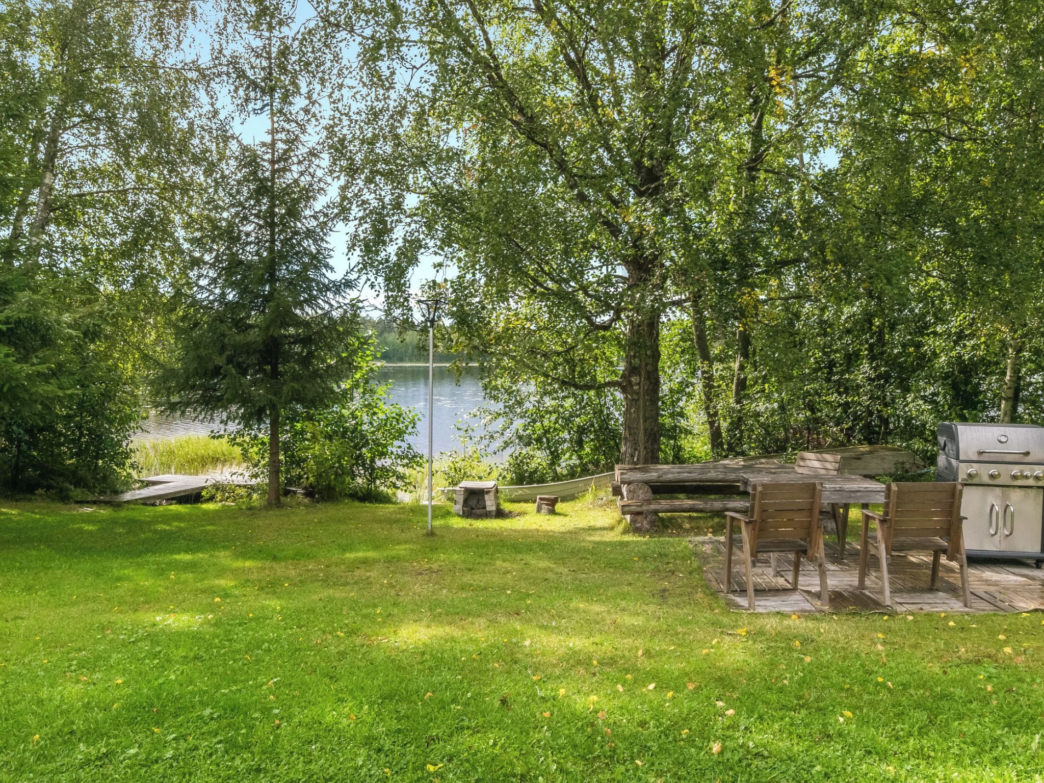 A grassy area with a picnic table, a grill, and a hammock near a body of water.