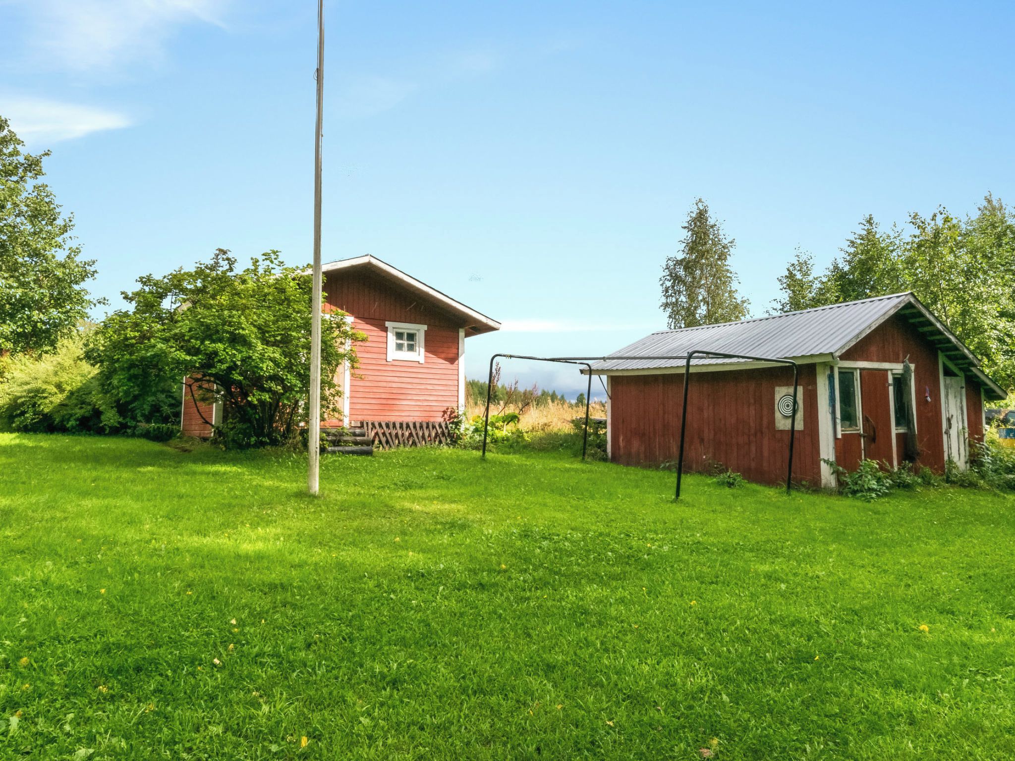 Une maison en bois rouge, avec un toit en métal et un portique à balançoire dans une cour verdoyante.
