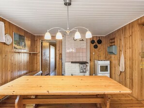 Puinen sisustus, jossa on suuri ruokapöytä, keittiöalue liedellä ja riippuvalaisin.