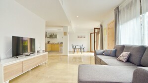 A modern living room with a flat-screen TV, grey sofa, and a dining area with a table and chairs.