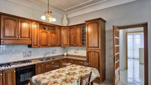 A kitchen with wooden cabinets, a gas stove, a sink, and a dining table with a floral tablecloth. - Mary's House, Agerola (Pianillo)