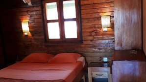 Una habitación de cabaña de madera con una cama, una mesita de noche y una mesilla auxiliar.