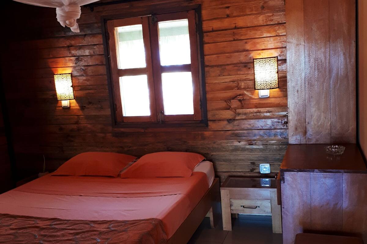 Una habitación de cabaña de madera con una cama, una mesita de noche y una mesilla auxiliar.