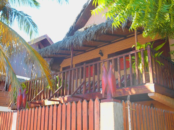 Un bâtiment en bois avec un toit de chaume, une clôture en bois et une végétation tropicale.