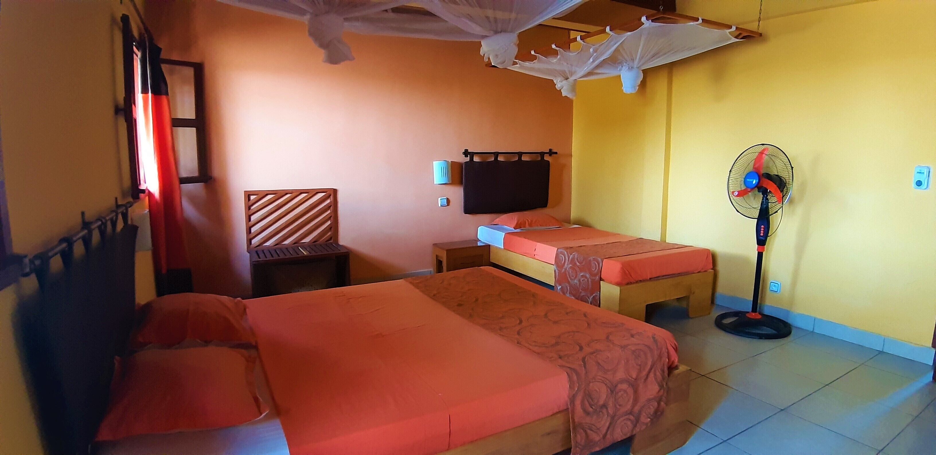 Een kamer met twee bedden, een stoel, een televisie, een ventilator en een klamboe.