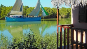 Un barco con dos velas en aguas tranquilas, una estructura de techo de paja y exuberante vegetación al fondo.
