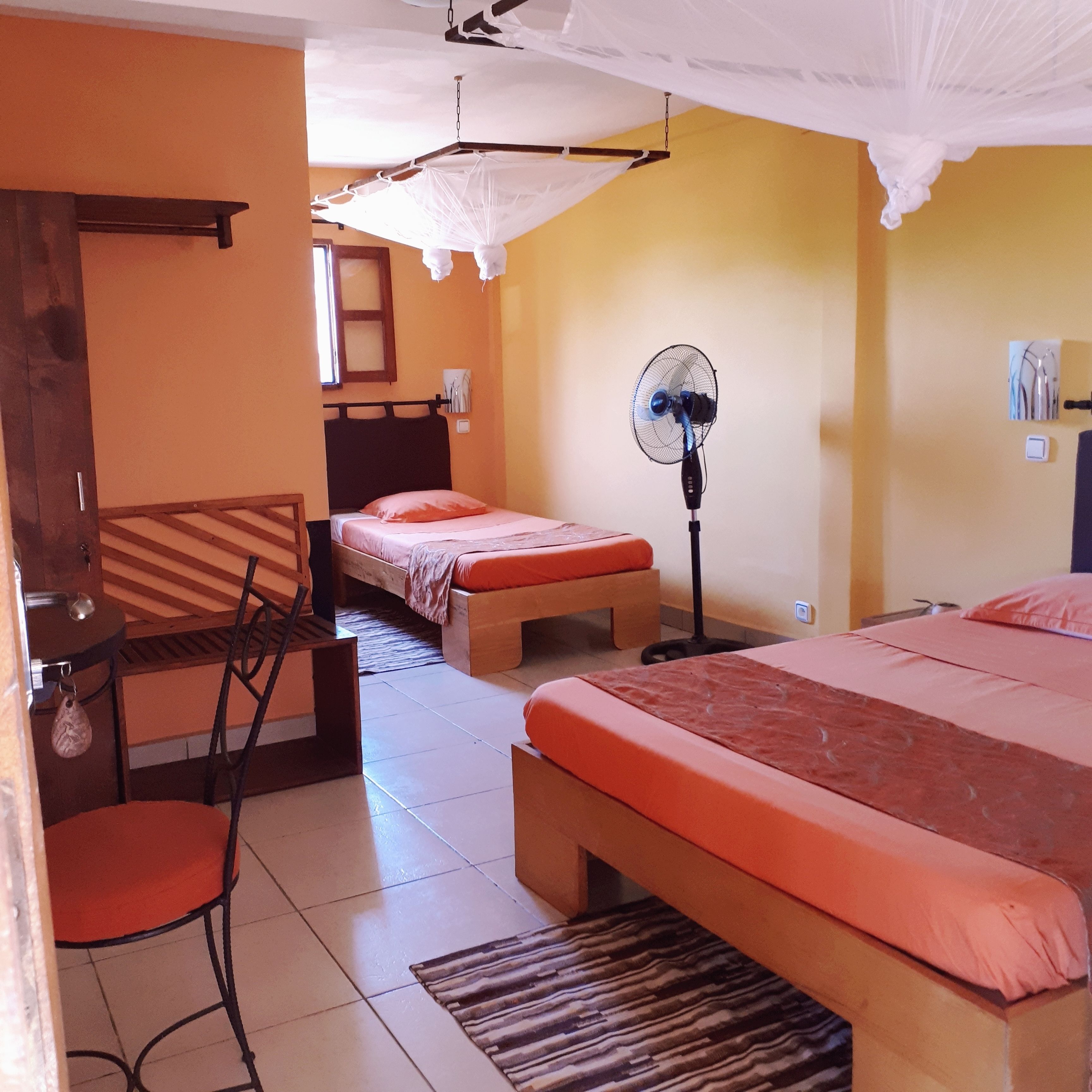 Een hotelkamer met twee bedden, een stoel, een bureau, een ventilator en een klamboe.
