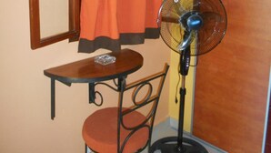 Una habitación pequeña con una mesa, una silla, un ventilador y una ventana con cortinas.