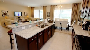 A modern kitchen with granite countertops, a central island, and a dining area with a chandelier. - New Listing! Solterra Resort, 7mi to Disney & 17mi to Universal - IT2630 (Davenport)