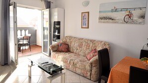 Una sala de estar con sofá, una mesa de centro de vidrio, una mesa de comedor con sillas, un cuadro en la pared y una puerta corrediza de cristal que da a un espacio exterior.