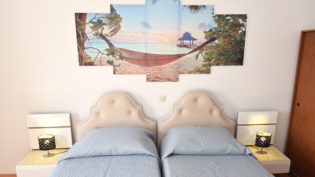 Un dormitorio con dos camas, una obra de arte en la pared que representa una escena de playa y lámparas de noche.