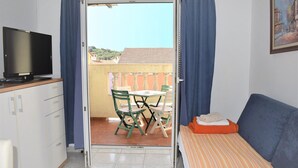 Una habitación pequeña con cama, televisión, mesa con sillas y balcón con vistas a edificios.
