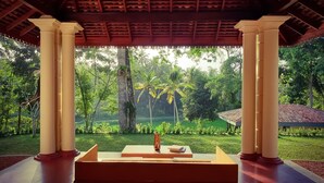 A covered outdoor seating area with a table and chairs, surrounded by lush greenery and palm trees. - The Mugatiya (Ahangama)