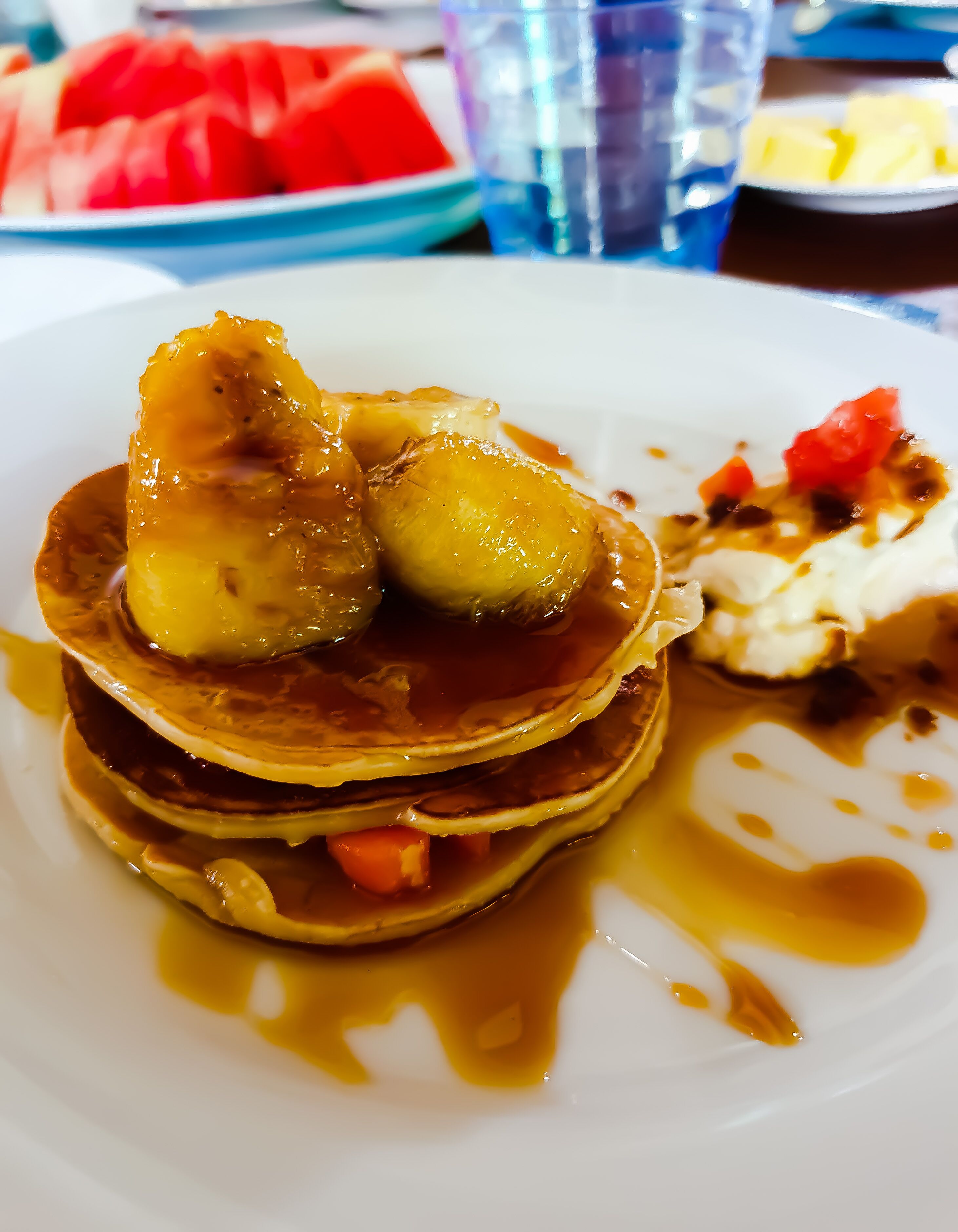 Ein Teller Pfannkuchen mit Sirup und Früchten auf weißem Geschirr.