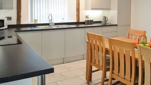 A modern kitchen with a built-in microwave, a sink, and a dining area with a wooden table and chairs. - 3 bedroom accommodation in Flamborough (Flamborough)