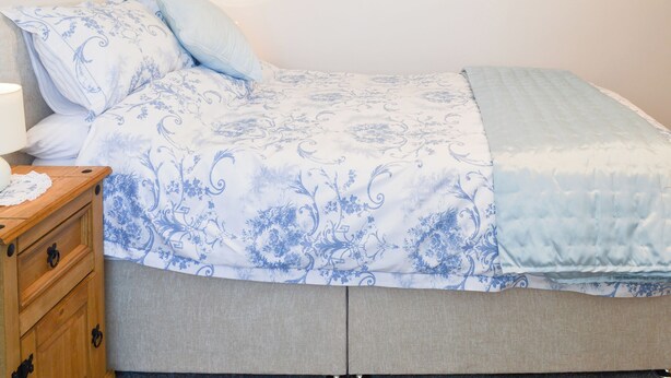 A bed with a floral patterned bedspread, a bedside table with a lamp, and a wooden nightstand with drawers. - 3 bedroom accommodation in Flamborough (Flamborough)