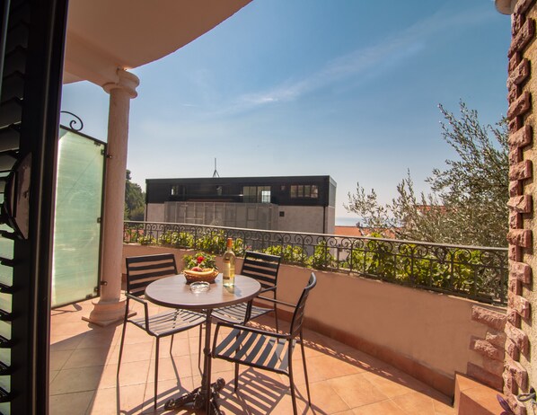 A balcony with a round table, chairs, and a bottle of wine.