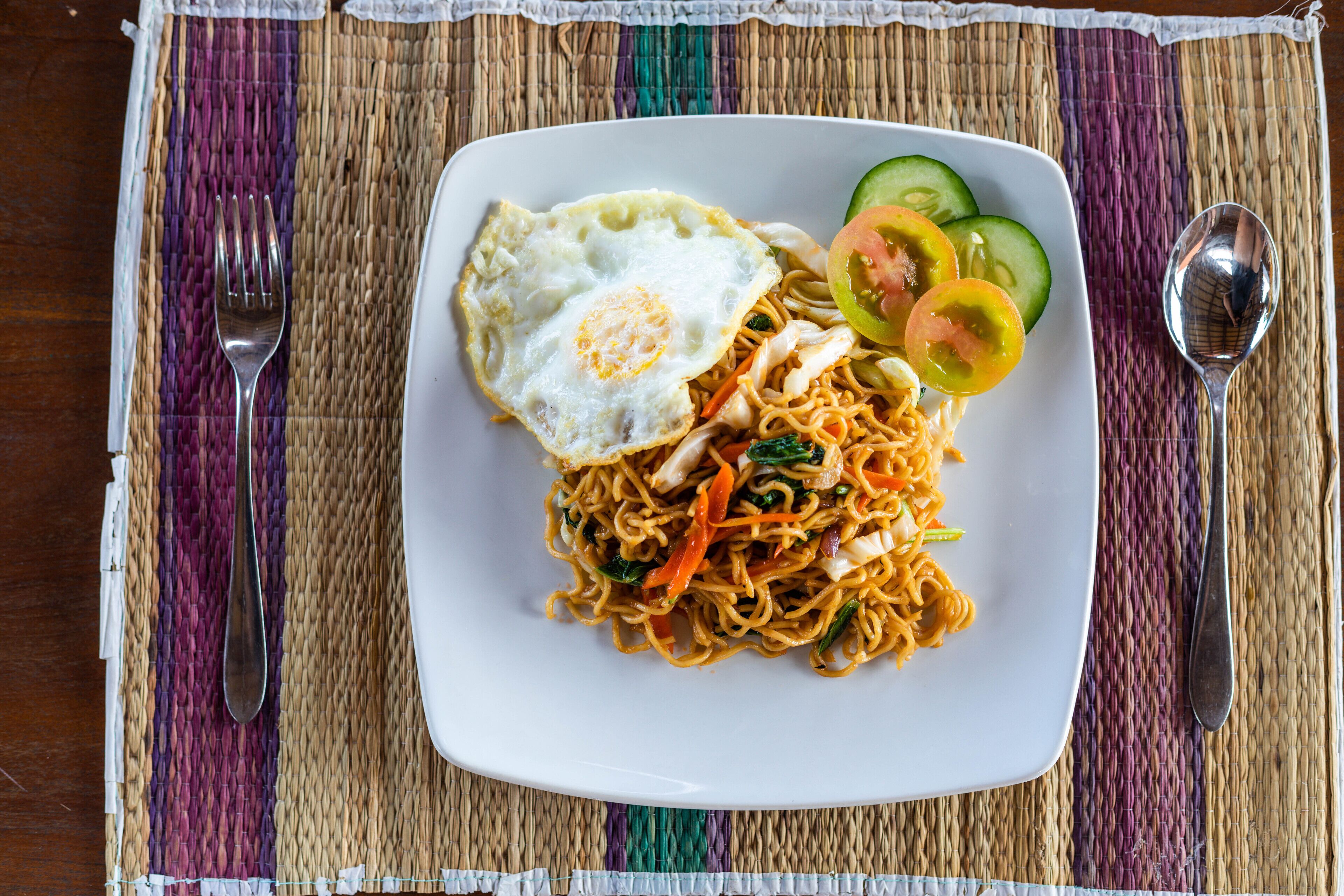 Un plato de fideos con verduras y un huevo frito sobre un plato blanco.