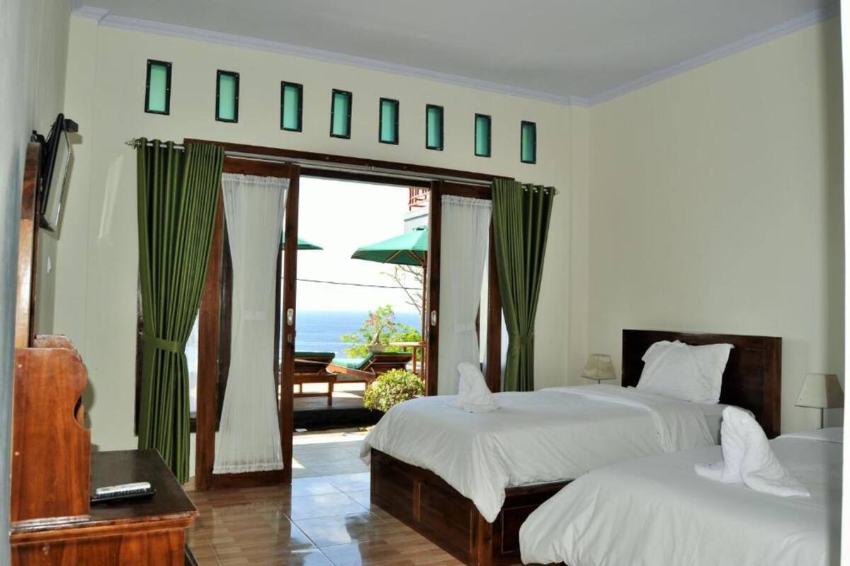 A hotel room with two beds, a wooden desk, and a view of the sea through a glass door.