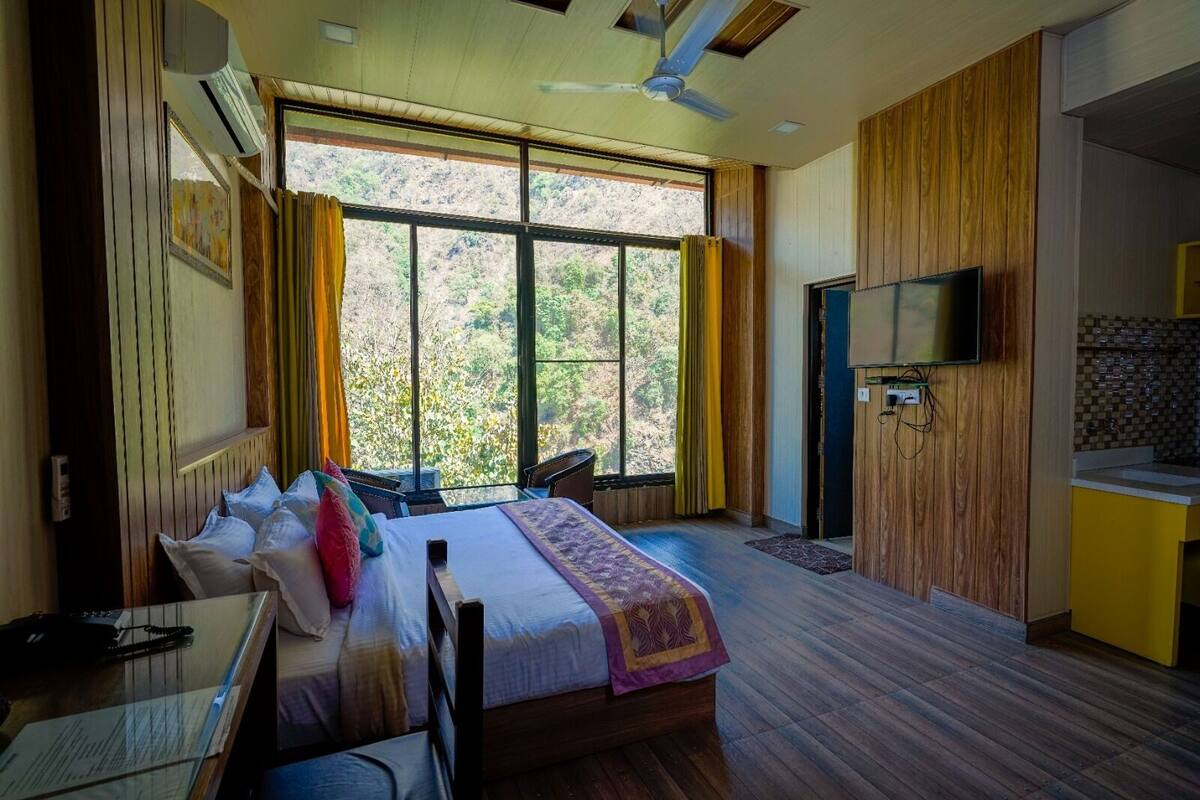 A bedroom with a bed, a desk, a chair, a TV, and a window with curtains.