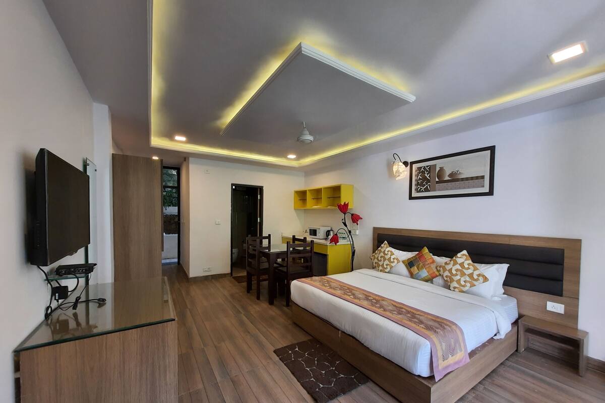 A modern hotel room with a large bed, a TV, a desk, and a dining area.