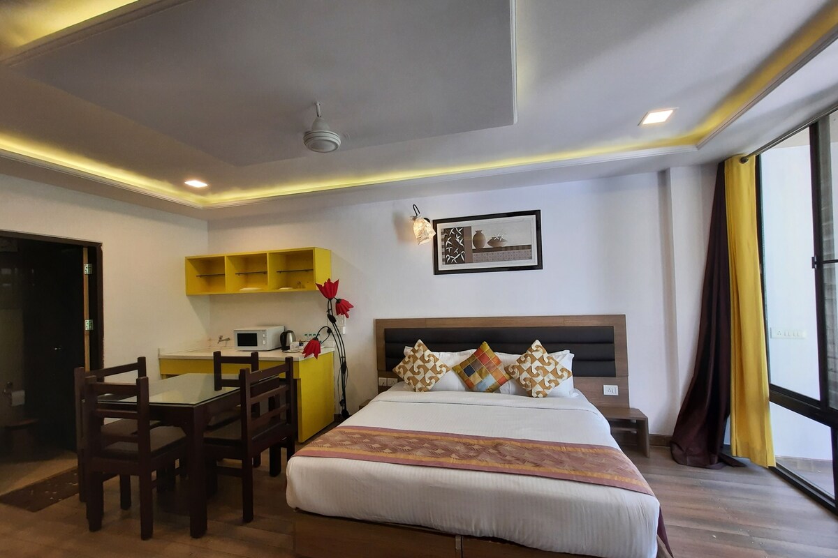 A hotel room with a bed, a desk, a chair, a microwave, and a small kitchenette.