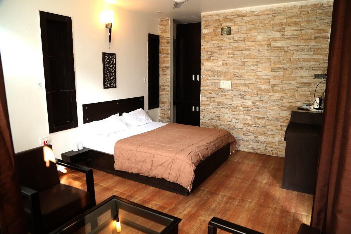 A hotel room with a bed, a desk, a chair, a stone wall, and a door.
