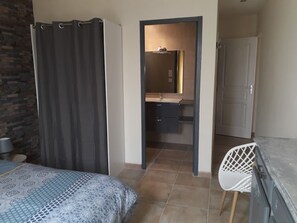 A bedroom with a bed, a chair, a wardrobe, and a bathroom with a mirror and sink. - Villa Lei Rigau (Salernes)