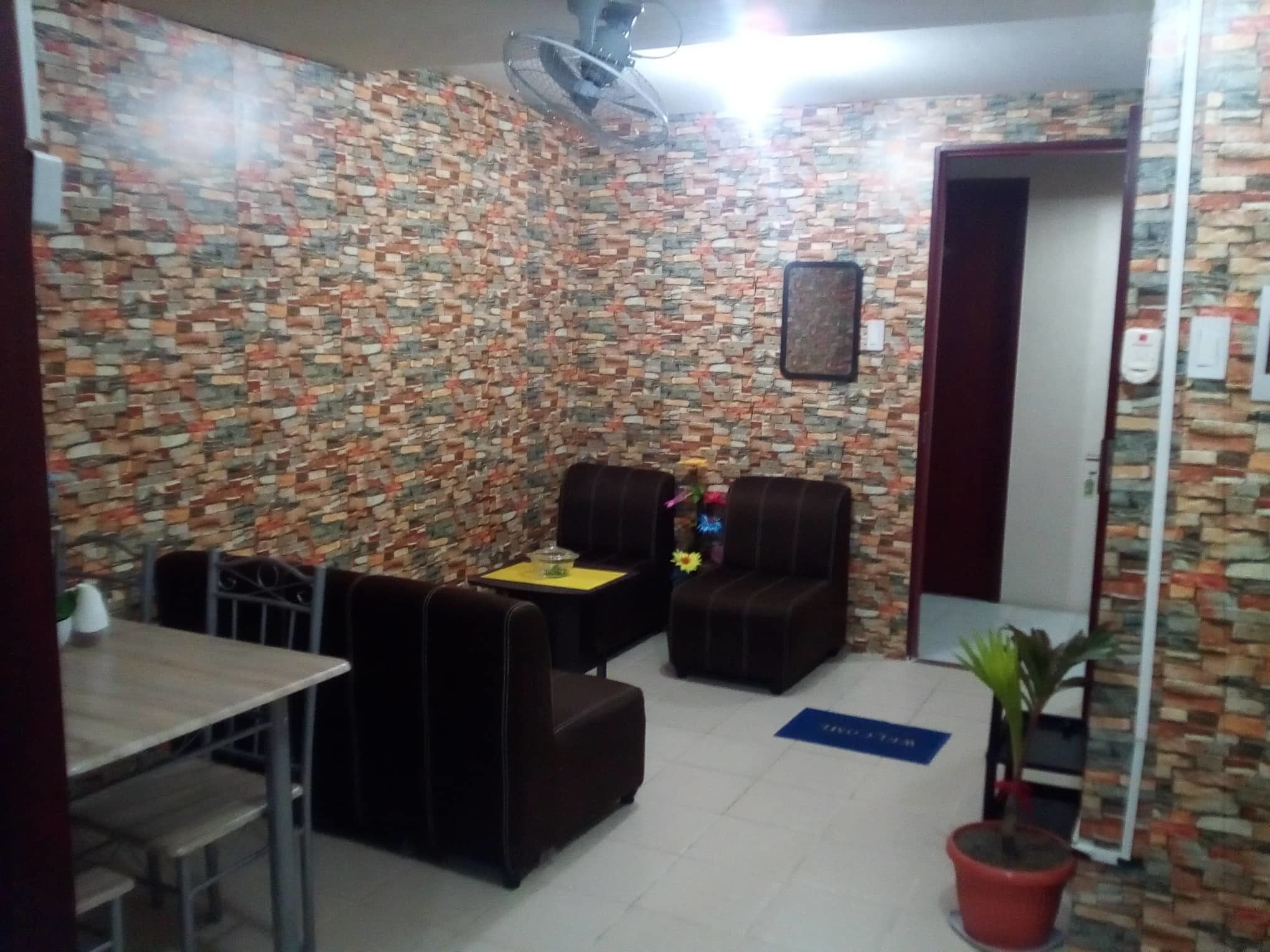 A room with a patterned wall, a table with chairs, a sofa, a potted plant, and a door.